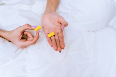 kadın yatakta oturuyor ve kulak tıkacı holding