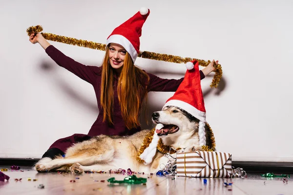 Щаслива жінка в різдвяному капелюсі сидить поруч з собакою на подарунковому фоні — стокове фото