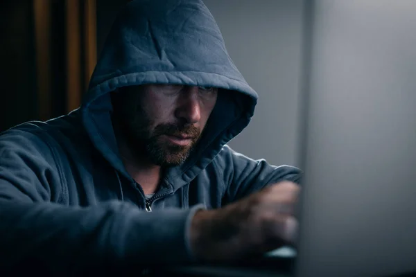 Hacker im Sweatshirt mit Kapuze sitzt hinter einem Laptop — Stockfoto
