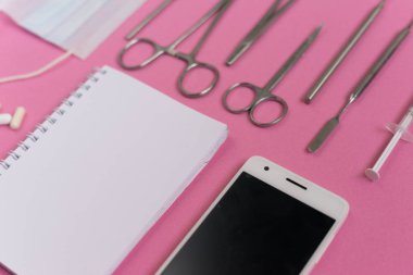 Pembe üzerinde beyaz bir akıllı telefon, defter ve diş aletleri yüzeydir