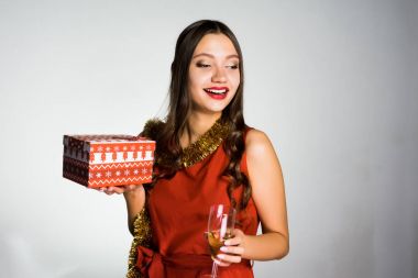 Kırmızı elbiseli güzel mutlu kız yeni yıl ve Noel kutluyor, cam şampanya ve hediye ile elinde tutan
