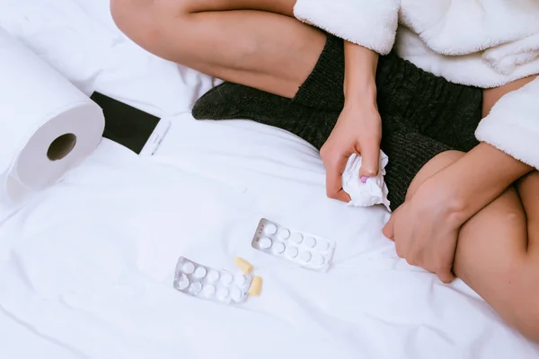 Дівчина в теплих шкарпетках сидить на ліжку, хвора, тримає таблетки — стокове фото