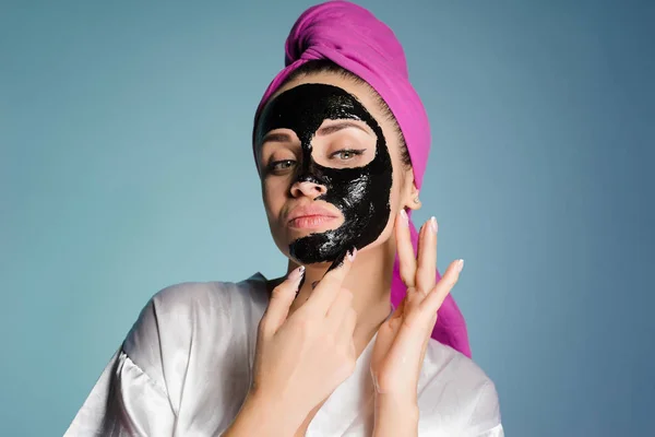 Fiatal, vonzó lány a fején rózsaszín törülközővel helyezi az arcán a fekete maszk, pattanások ellen — Stock Fotó