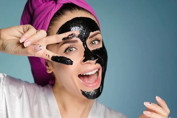 Όμορφη νεαρή κοπέλα με μια ροζ πετσέτα στο κεφάλι της, το γέλιο, στο πρόσωπό της μια μαύρη μάσκα που δείχνει δύο δάχτυλα — Φωτογραφία Αρχείου