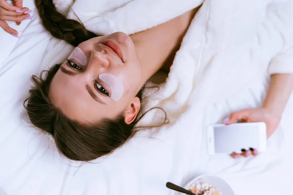 Młoda dziewczyna w białą szatę leży na łóżku, pod oczy białe plamy — Zdjęcie stockowe