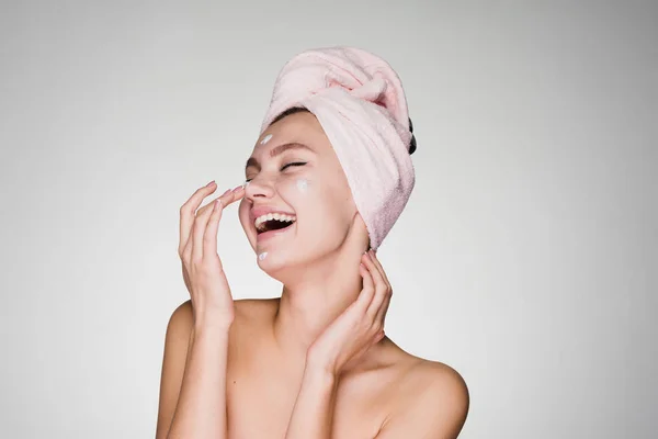 Mulher feliz com uma toalha na cabeça aplicando creme no rosto — Fotografia de Stock