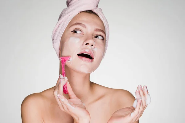 Kvinna med en handduk på huvudet gör en ansikts hårborttagning med ett rakblad — Stockfoto