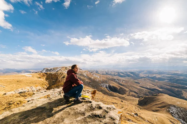 Turista donna si siede su una scogliera sullo sfondo delle montagne in una giornata di sole — Foto Stock