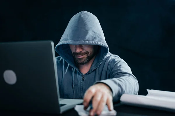 Homem hacker sentado na mesa olhando para o laptop e, em seguida, digitando e sorrindo — Fotografia de Stock