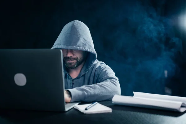 Homem hacker sentado à mesa olhando para laptop e sorrindo — Fotografia de Stock
