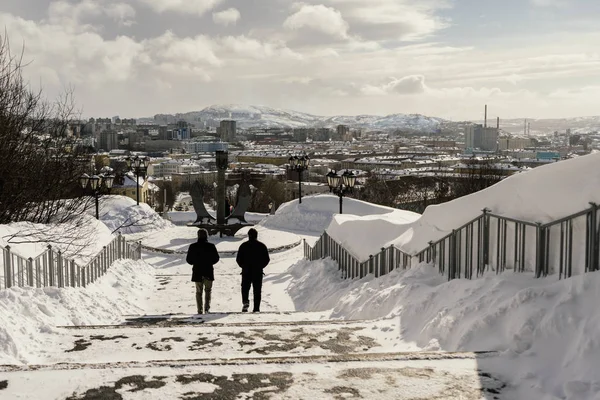 People go down the snow-covered stairs against the backdrop of the city — Stock Photo, Image