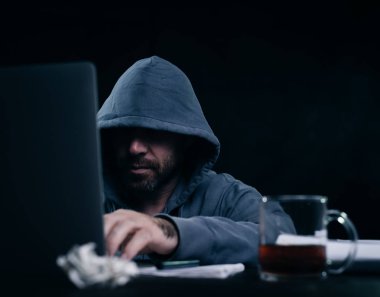 bir kazak bir masada oturan ve laptop arıyorum bir kukuleta ile erkek hacker