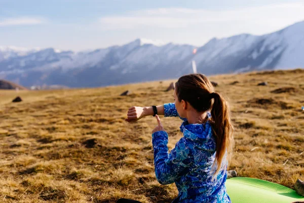 Женщина турист смотрит на фитнес-браслет на фоне гор в солнечный день — стоковое фото