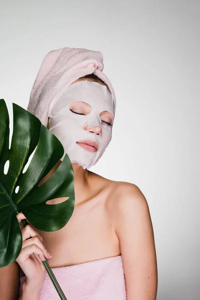 Een vrouw met een handdoek op haar hoofd zetten een masker op haar gezicht en staat met haar ogen dicht — Stockfoto