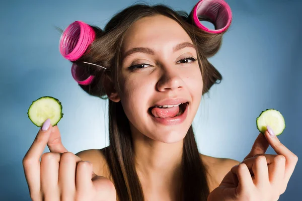 Mulher feliz com grandes encrespadores na cabeça segura um pepino — Fotografia de Stock