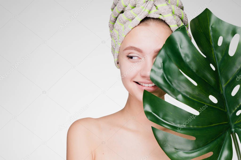 happy woman with a towel on her head covered her face with a green leaf and looks away