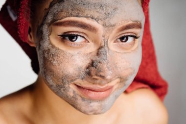 Kafasındaki bir havlu ile güzel bir genç kız onun yüzüne bir kil maskesi uygulanmış, güzel olmak istiyor