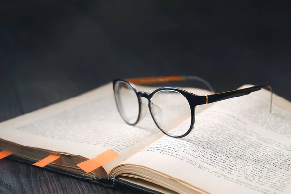 Σε ένα σκοτεινό ξύλινο πάτωμα είναι ένα βιβλίο με γυαλιά και σελιδοδείκτες — Φωτογραφία Αρχείου