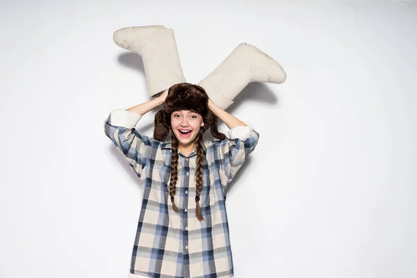 Rusa riendo chica en un sombrero con orejeras sostiene valenki — Foto de Stock