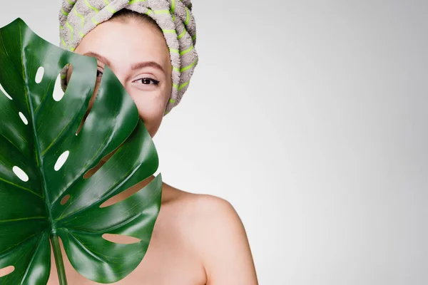 Linda joven disfrutando de tratamientos de spa, sosteniendo una hoja verde, con una toalla en la cabeza — Foto de Stock