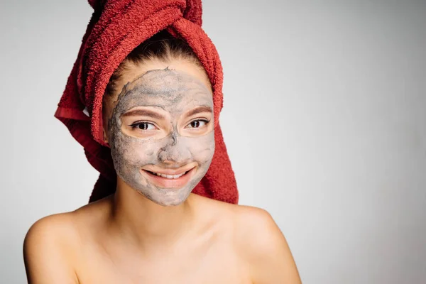 美丽的微笑女孩用毛巾在她的头上应用了一个有用的粘土面具在她的脸上 — 图库照片