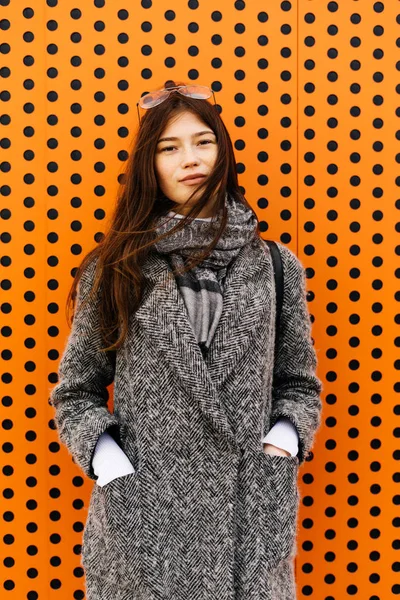 Стильна модна дівчина в сірому пальто позує на помаранчевому фоні, зовнішня мода — стокове фото