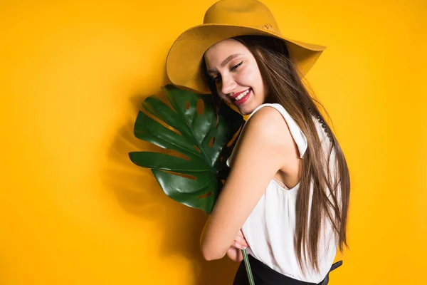 Feliz chica de pelo largo en un sombrero de moda sostiene una hoja verde, se ríe — Foto de Stock