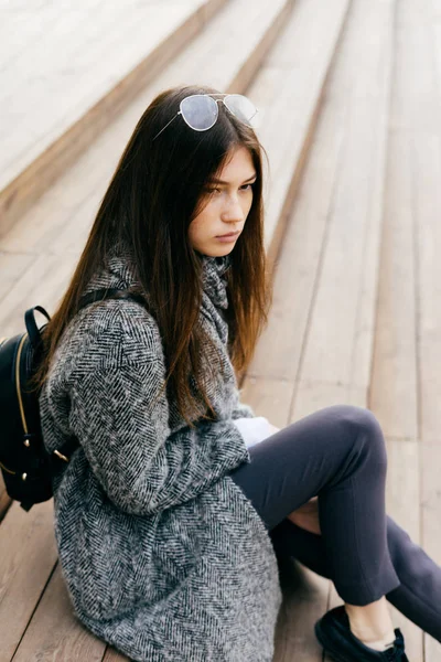 Stylish girl in fashionable clothes and glasses sits on the steps in the open air, street style — Stock Photo, Image