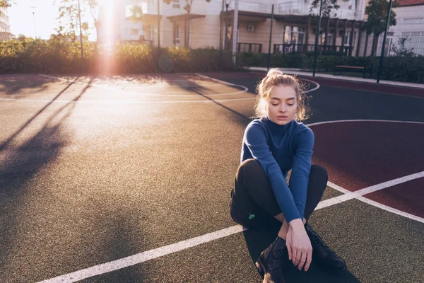 Mooi blond meisje zit op de grond buiten in de zon, in de stijlvolle kleding — Stockfoto
