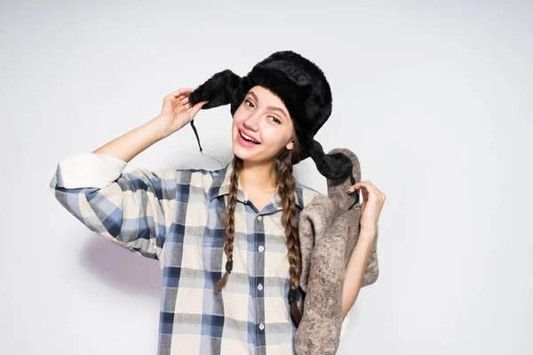 Feliz joven rusa chica en un sombrero con orejeras sostiene botas de fieltro gris en las manos — Foto de Stock