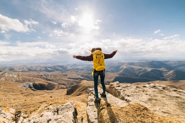 Active young girl with a yellow backpack travels through the Caucasus mountains, enjoys nature, raised her hands upwards — Stock Photo, Image