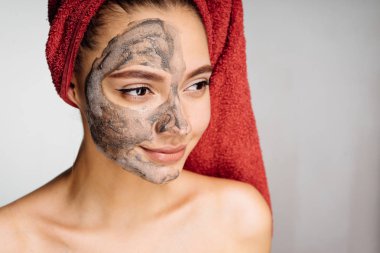 başında kırmızı bir havlu ile çok hoş bir genç kız için yarım yüz yararlı kil maskesi uygulanmış