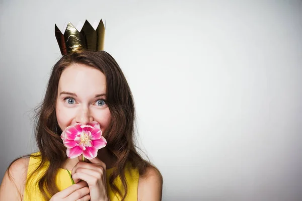 Glad ung flicka med en gyllene krona på hennes huvud som firar en internationella kvinnodagen, hålla en doftande rosa blomma — Stockfoto