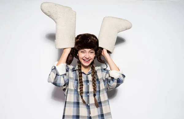 Feliz chica rusa en un sombrero caliente con orejeras sostiene botas de fieltro gris en las manos — Foto de Stock
