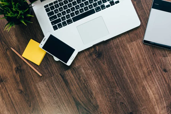 Op de houten vloer is een laptop en een smartphone, geel papier en potloden — Stockfoto