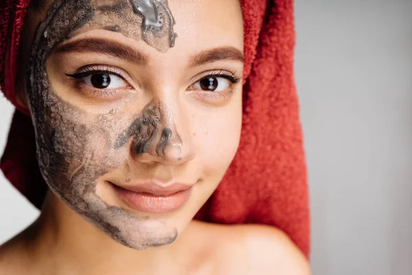 Kafasındaki bir havlu ile sevimli bir genç kız yüzünü bir kil maskesi koymak sonra görünüyor