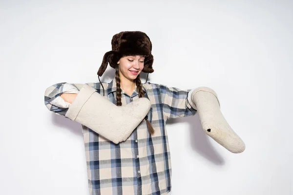 Divertida joven en un sombrero con orejeras sostiene botas de fieltro caliente en las manos — Foto de Stock