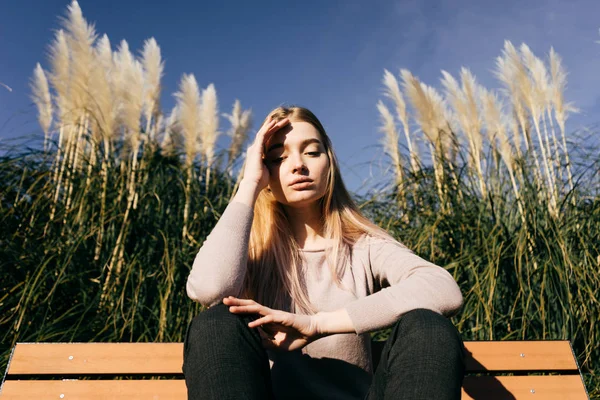 緑の野原の背景に太陽の下で座っているスタイリッシュな服でかわいい若いブロンドの女の子 — ストック写真