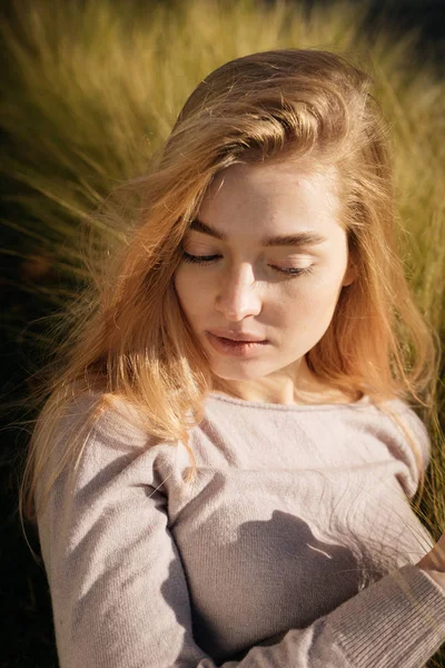 Giovane ragazza carina con i capelli biondi seduta in un campo al sole, in posa — Foto Stock