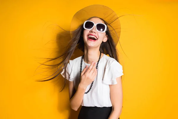 Felice ragazza elegante in cappello di moda e occhiali da sole in posa contro sfondo muro giallo, ridendo — Foto Stock