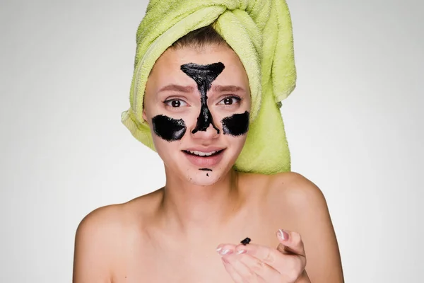 Divertente ragazza con un asciugamano verde sulla testa si mette una maschera nera contro l'acne sul viso — Foto Stock