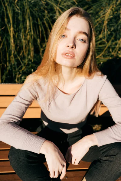 Joven hermosa modelo chica con pelo rubio con ojos azules sentado en un banco, posando — Foto de Stock
