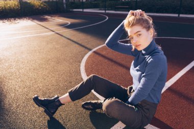 genç güzel sarışın model kız sokak stili bir spor sahasında oturuyor