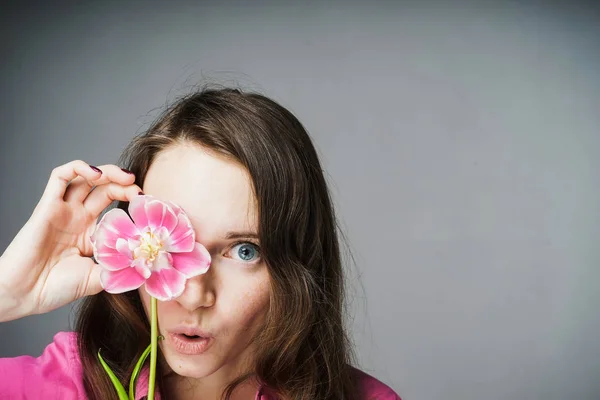 Sorprendida hermosa joven con una camisa rosa celebra el día mundial de la mujer, sostiene una flor rosa — Foto de Stock