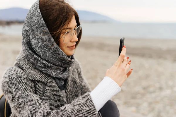 Stylish young girl with a gray scarf and glasses takes pictures of a beautiful street — Stock Photo, Image