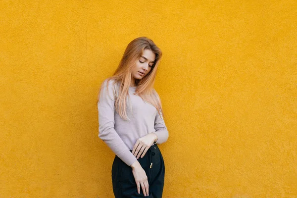 Eleganta slanka tjej blond i en vit jacka poserar mot en gul vägg — Stockfoto