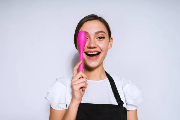 Щаслива усміхнена дівчина готує в чорному фартусі тримає рожеву ложку — стокове фото