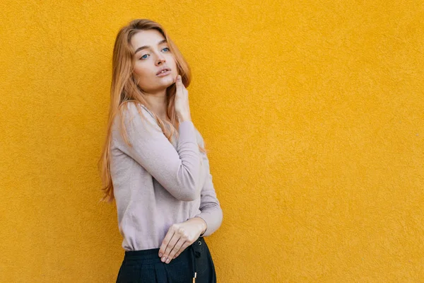 Joven hermosa chica con el pelo rubio posando contra la pared amarilla, mirando a la distancia — Foto de Stock