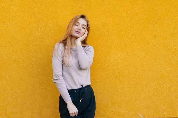 Linda joven rubia puso su mano en su cara, sonriendo, posando sobre un fondo amarillo de la pared — Foto de Stock