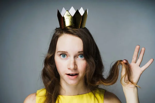 Hermosa joven sorprendida con una corona de oro en la cabeza sostiene un rizo de pelo en la mano — Foto de Stock